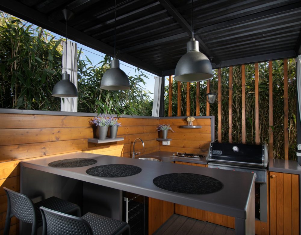 An open-air mini kitchen with wooden parts, trees and sky background
